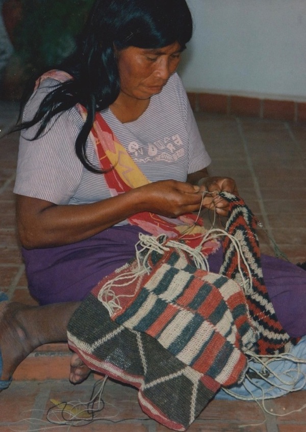 Mujer sentada en el suelo tejiendo una bolsa de mano.